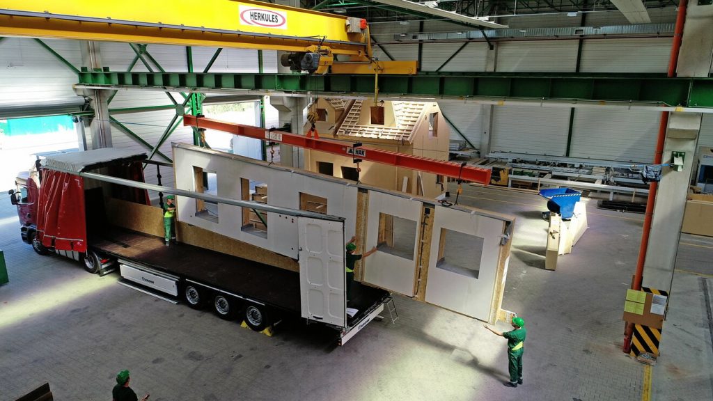 A pre-fabricated wall of a building - fully insulated, with holes cut for windows - loaded onto back of lorry for transporting.